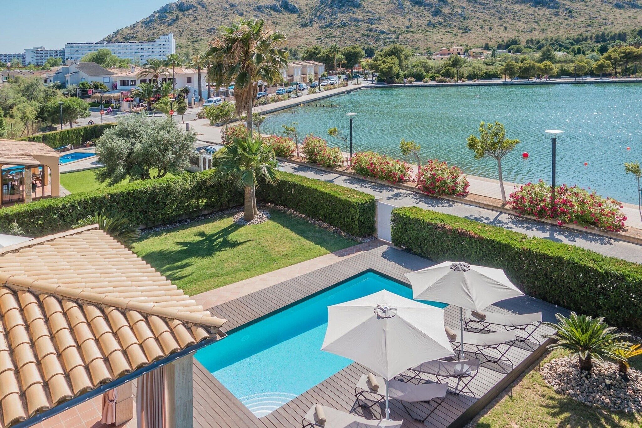 A swimming pool with a wooden deck, surrounded by neatly trimmed hedges and palm trees.