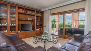 A living room with leather sofas, a glass coffee table, a flat-screen TV, and a bookshelf filled with books and decorative items. - Waterfront Port d'Alcudia Villa for 8 (Port d´Alcudia)