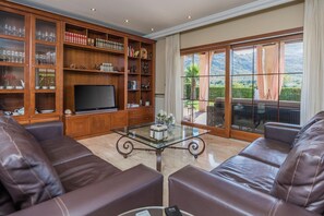 A living room with leather sofas, a glass coffee table, a flat-screen TV, and a bookshelf filled with books and decorative items. - Waterfront Port d'Alcudia Villa for 8 (Port d´Alcudia)