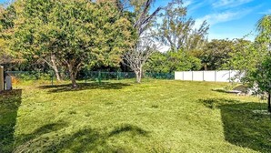A well-maintained grassy yard with trees and a fence. - Cape Coral Pool Home Near Tarpon Point (Cape Coral)