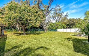 A well-maintained grassy yard with trees and a fence. - Cape Coral Pool Home Near Tarpon Point (Cape Coral)