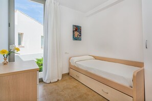 A bedroom with a bed, a desk, a painting, and a window with curtains. - Seaside Escape in Cala Sant Vicenç (Cala Sant Vicenç)