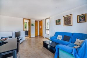 A modern living room with a blue sofa, a flat-screen TV, and a coffee table. - Seaside Escape in Cala Sant Vicenç (Cala Sant Vicenç)