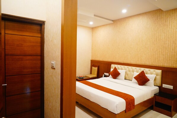 Habitación de hotel con armario de madera, cama con ropa de cama blanca y detalles marrones, y mesita de noche con lámpara.