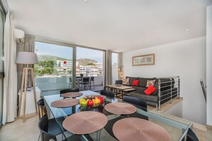A modern living room with a glass dining table, black sofas, and a city view.