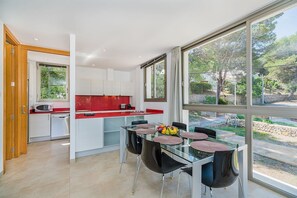 A modern kitchen with a glass dining table and chairs, a red countertop, and a view of the outdoors.