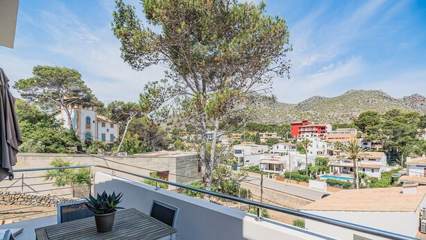 A balcony with a table and chairs, overlooking a residential area with houses and a mountain in the background. - Beachside Escape in Cala Molins (Cala Sant Vicenç)