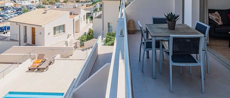 A balcony with a pool, a dining area with chairs and a table, and a view of the sea and buildings in the background.