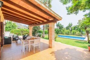 Eine Terrasse im Freien mit einem Esstisch, Stühlen und einem Pool im Hintergrund.