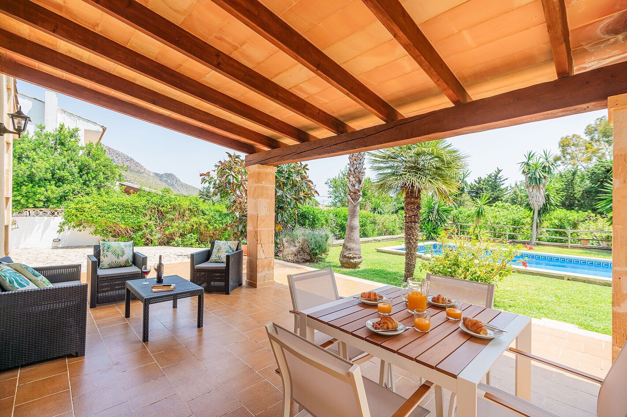 Eine Terrasse im Freien mit einer Holzpergola, Korbmöbeln und einem Esstisch, gedeckt für das Frühstück.