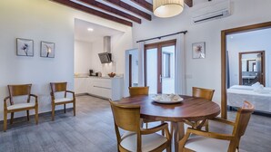 A dining area with a round wooden table and four chairs, a kitchen in the background, and a large window with curtains. - Central House with Pool, Puerto Pollença (Port de Pollença)