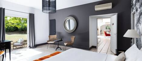 Habitación de hotel moderna con una cama grande, un área de comedor con sillas, un espejo redondo y vistas al exterior.