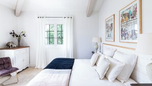 A bedroom with a bed, a dresser, a chair, a window with curtains, and wall art. - L’Orangerie – chic country house with pool, and child friendly gardens (Blauzac)