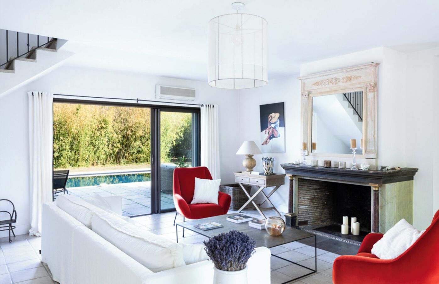Ein modernes Wohnzimmer mit einer Couch, roten Sesseln, einem Kamin und Blick auf einen Swimmingpool.