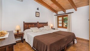 A bedroom with a wooden bed, bedside lamps, a window with curtains, and a wall-mounted air conditioner. - Mountain Villa with Large Pool (Pollensa / Pollença)