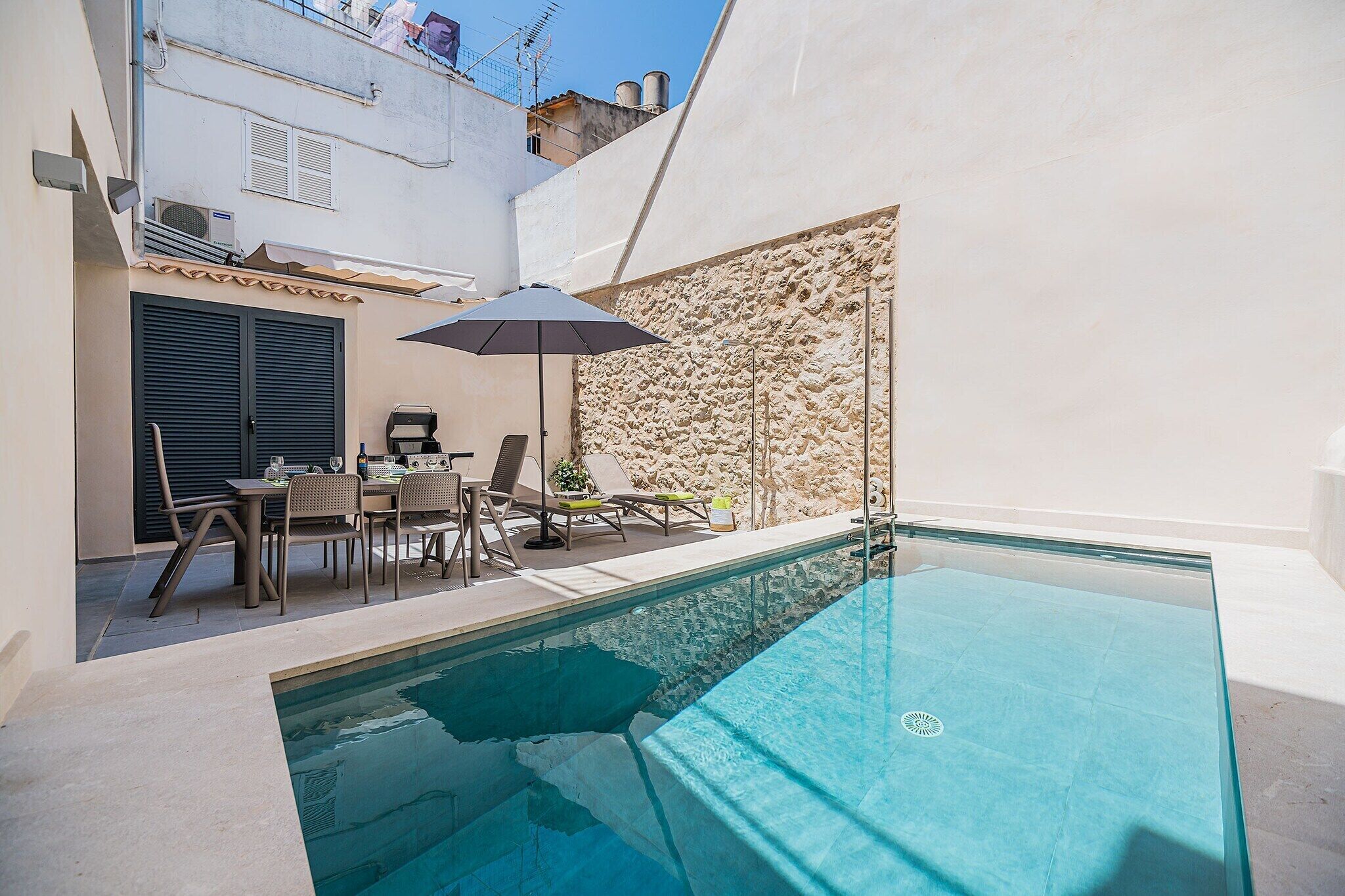 Piscina com muro de pedra e mesa com cadeiras.