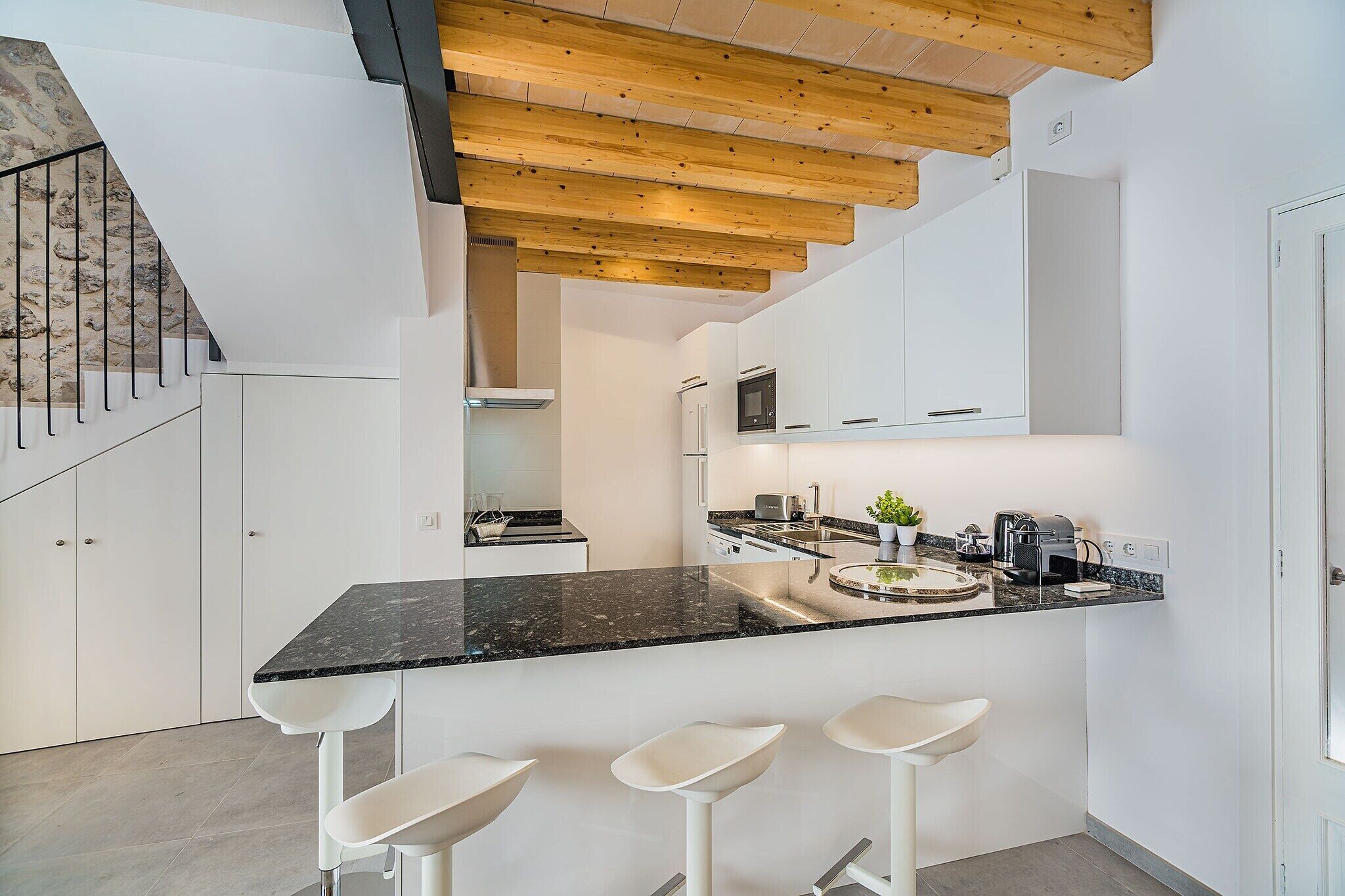 A modern kitchen with a central island, white cabinetry, and a wooden ceiling.