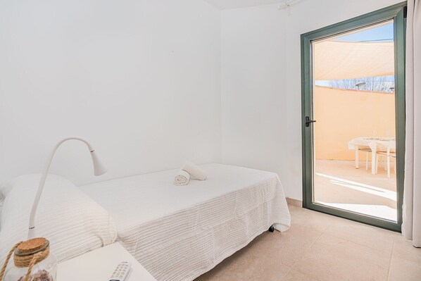 Un dormitorio con cama, mesita de noche, lámpara y vista a un patio exterior.
