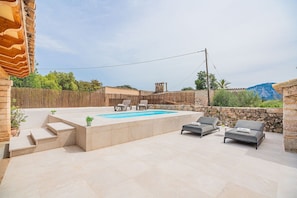 A pool area with a stone wall, lounge chairs, and a small table. - Cosy 2-Bed Villa with Pool, Pollença (Pollensa / Pollença)
