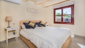 A bedroom with a bed, bedside tables, a lamp, a window, and an air conditioning unit. - 3-Bed Villa with Pool, Puerto Pollença (Puerto Pollensa)