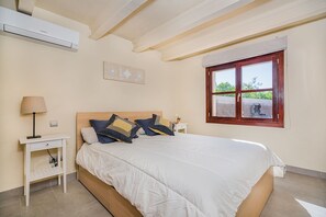 A bedroom with a bed, bedside tables, a lamp, a window, and an air conditioning unit. - 3-Bed Villa with Pool, Puerto Pollença (Puerto Pollensa)