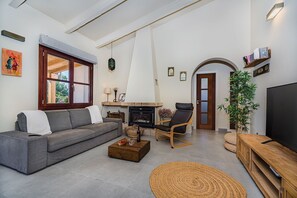 A living room with a sofa, a fireplace, a television, and a bookshelf. - 3-Bed Villa with Pool, Puerto Pollença (Puerto Pollensa)
