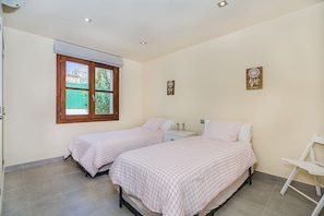 A bedroom with two beds, a window with a view, and a small bedside table with a lamp. - 3-Bed Villa with Pool, Puerto Pollença (Puerto Pollensa)