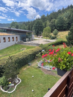 A modern building with a glass facade, a well-maintained garden with hedges and flowers, and a view of a forested hill. - Spacious Vacation Rental in the Upper Black Forest with an Infrared Sauna & South-Facing Balcony (Sankt Blasien)