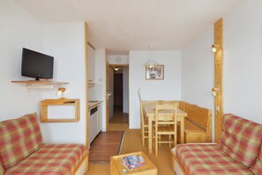 A compact living space with a television, a kitchenette, a dining area, and a small hallway leading to another room. - travelski home classic - Résidence Themis - 2 pièces 4/5 personnes (La Plagne)