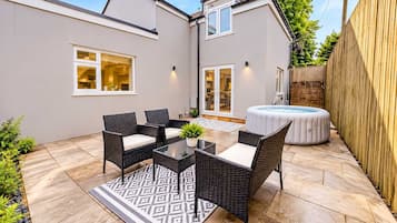 A patio with wicker furniture, a hot tub, and a patterned rug.