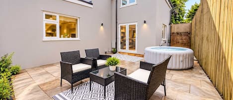 A patio with wicker furniture, a hot tub, and a patterned rug.