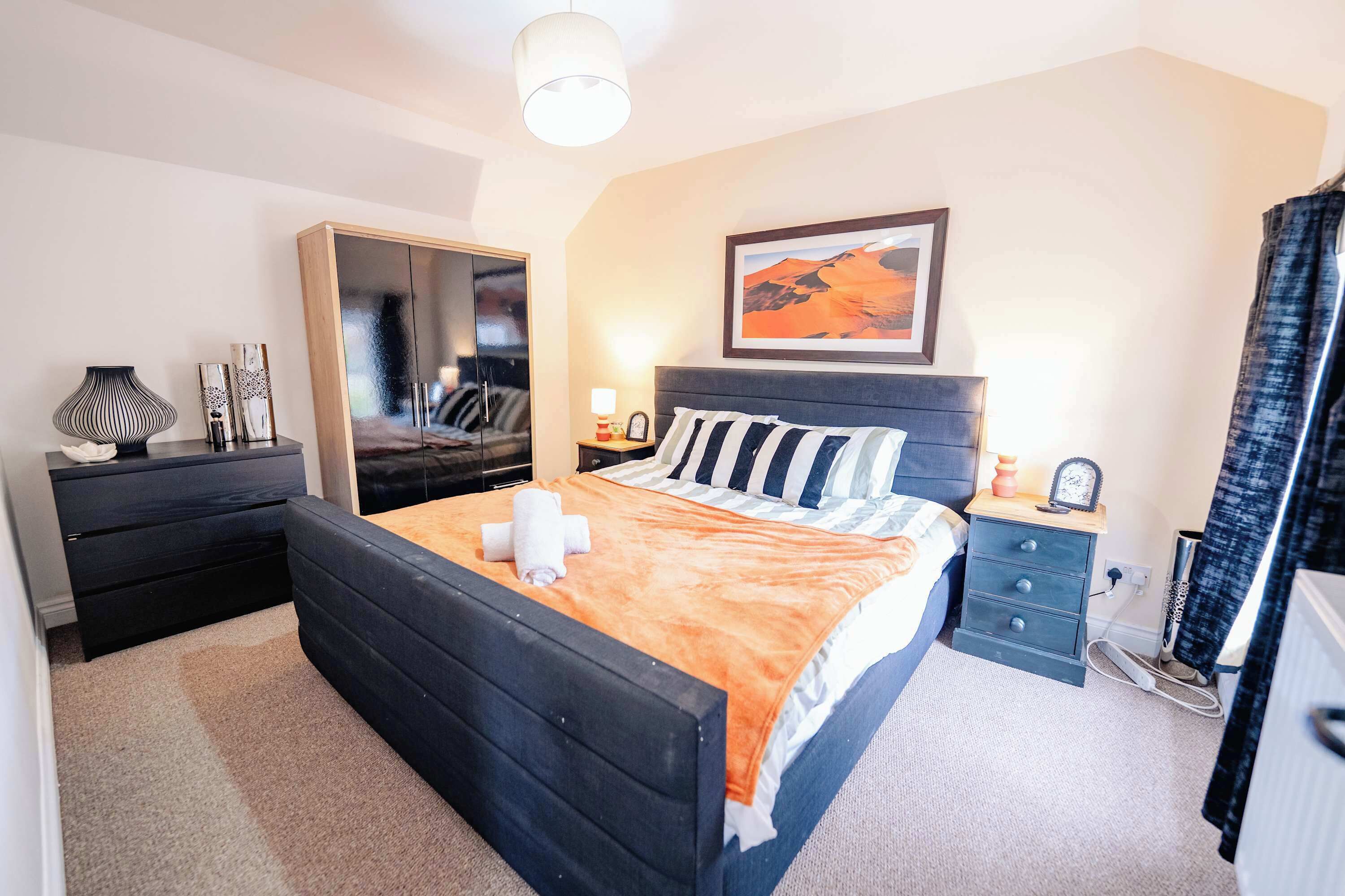 A bedroom with a bed, a dresser, a nightstand, a mirror, and a painting on the wall.