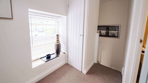Ein Flur mit einer Tür, einem Fenster mit Jalousien, einer Vase und einem gerahmten Bild an der Wand.