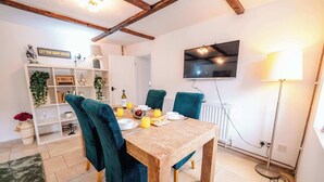 Ein Essbereich mit einem Holztisch, stuhlfarbenen Stühlen und einem an der Wand befestigten Fernseher.