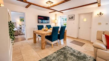 A dining area with a wooden table and blue chairs, a TV displaying Netflix, and a cozy living room with a sofa and a door.