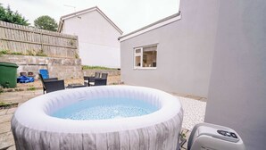 Ein Whirlpool im Freien mit Holzverkleidung, eine Terrasse mit Stühlen und ein Haus im Hintergrund.