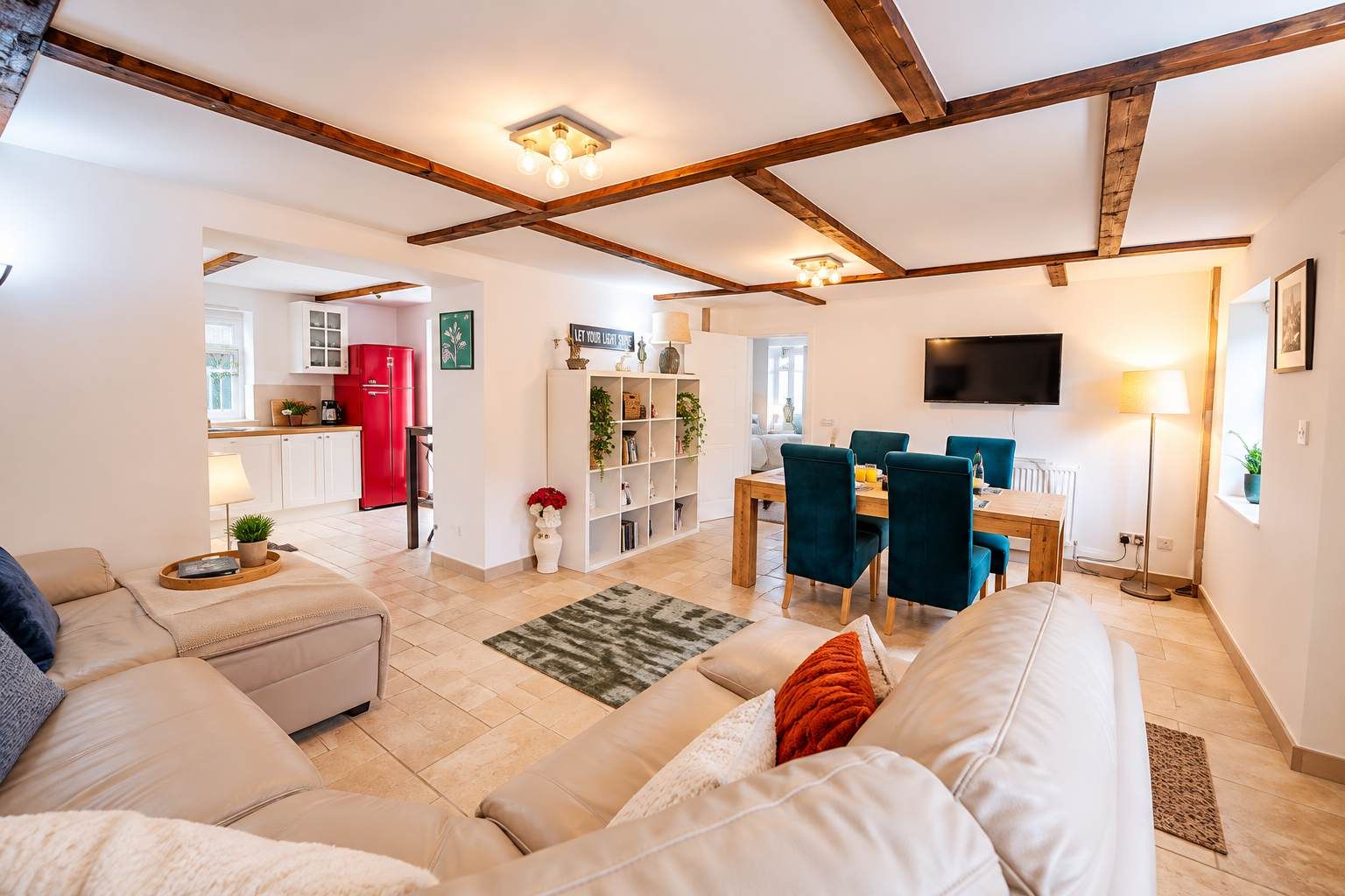 A modern living room with a sofa, a dining area with chairs, a kitchen in the background, and exposed wooden beams on the ceiling.