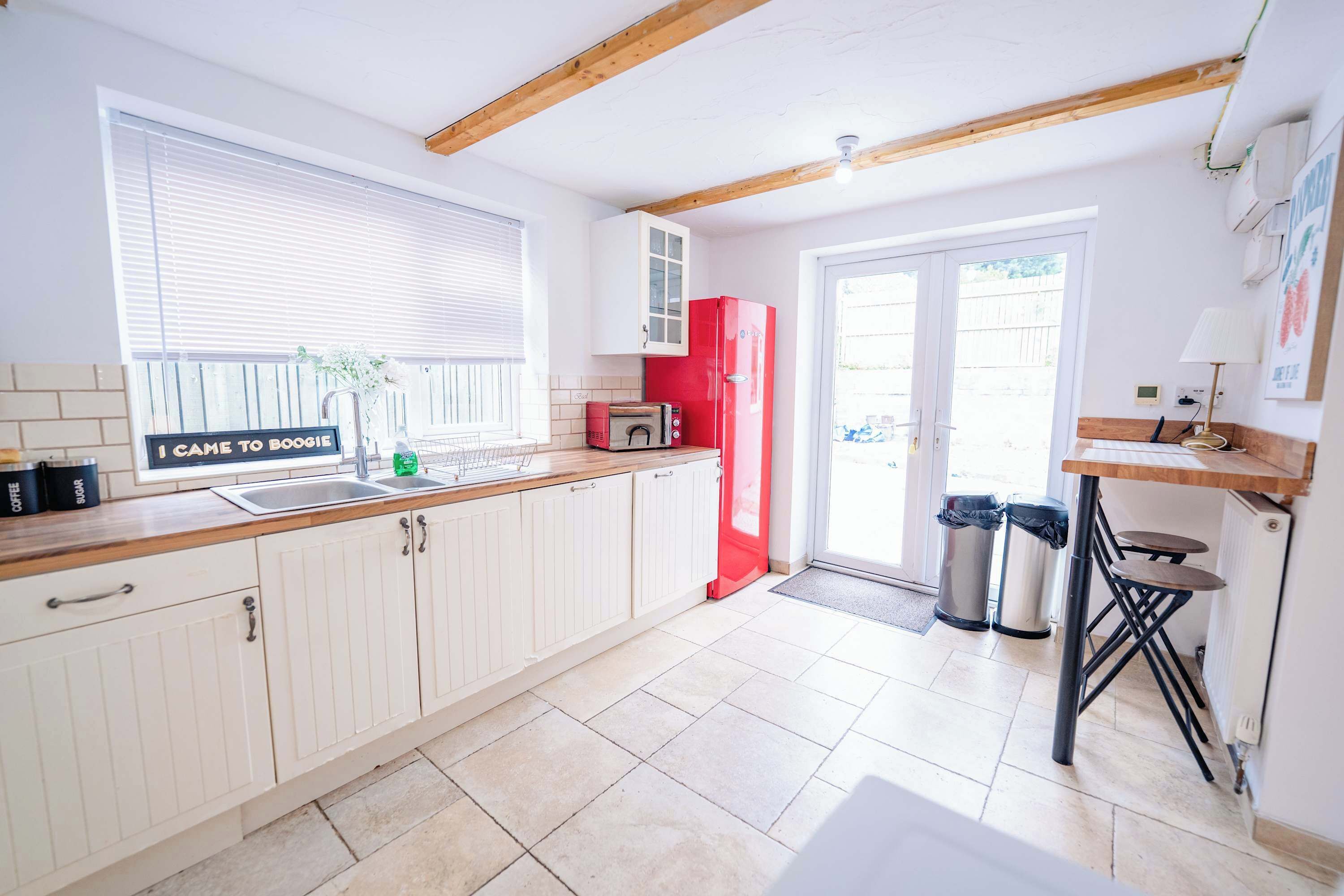 A kitchen with white cabinets, a red refrigerator, and a window with blinds.
