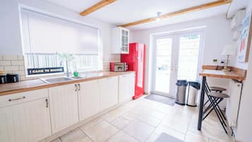 A kitchen with white cabinets, a red refrigerator, and a window with blinds.