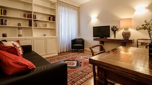 En stue med en sort lædersofa, et træspisebord, et fjernsyn og en reol.