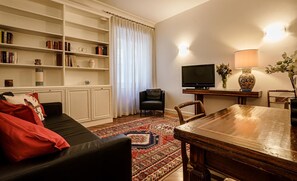 Ein Wohnzimmer mit einem schwarzen Ledersofa, einem Holzessttisch, einem Fernseher und einem Bücherregal.