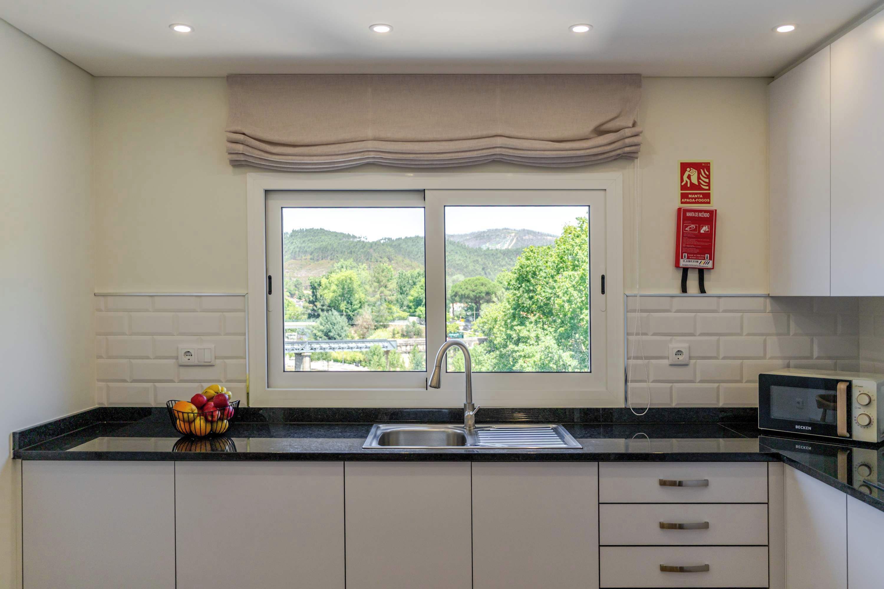 A kitchen with a double sink, a microwave, and a fruit bowl on the counter.