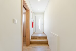 A narrow hallway with wooden flooring, a white door at the end, and a fire extinguisher mounted on the wall.