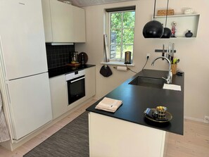 Eine moderne Küche mit weißen Schränken, einer schwarzen Arbeitsplatte, einem eingebauten Backofen, einem Fenster mit Ausblick und einer Spüle mit Geschirr.