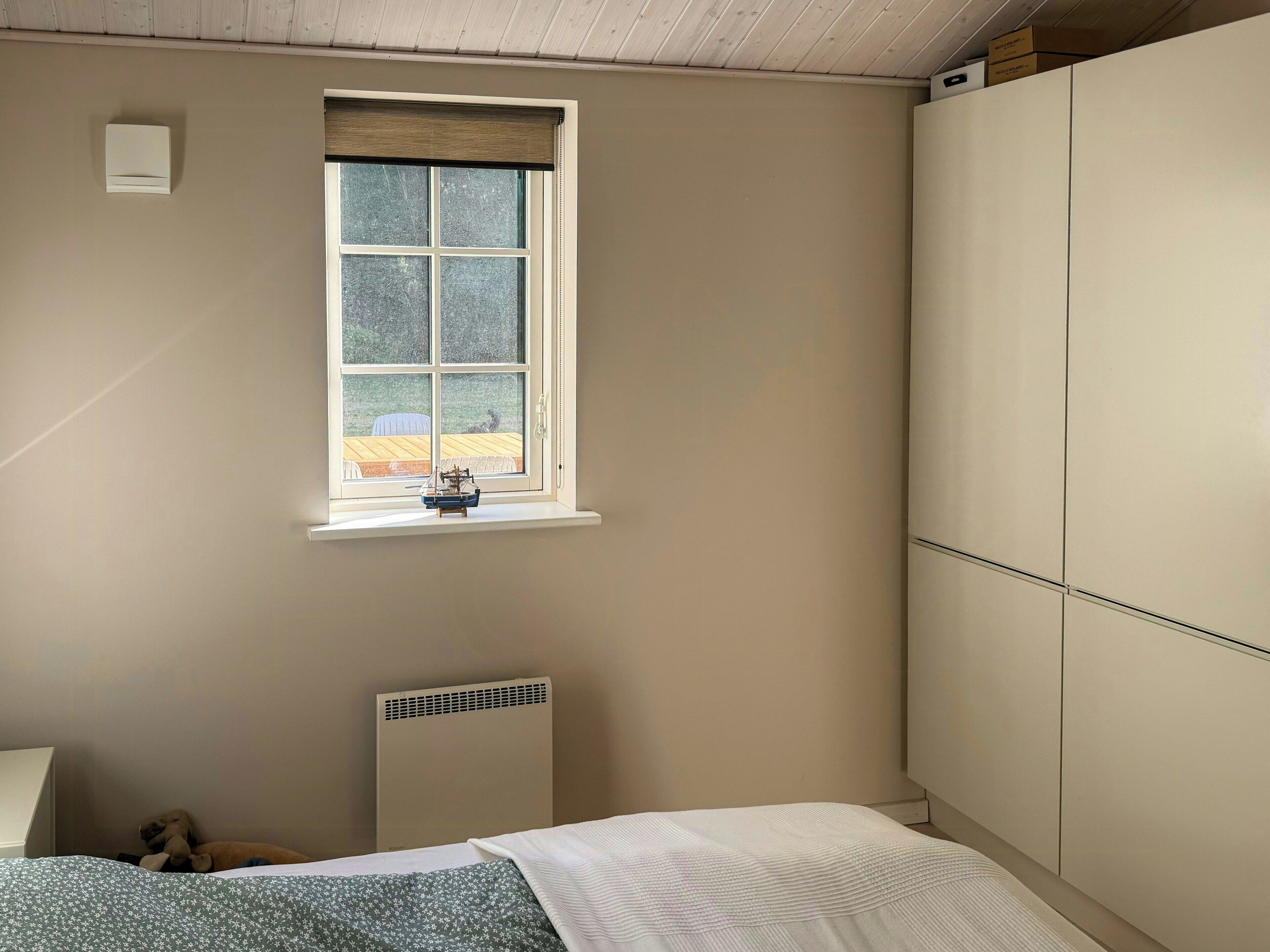 Een slaapkamer met raam, radiator, bed en een kledingkast.