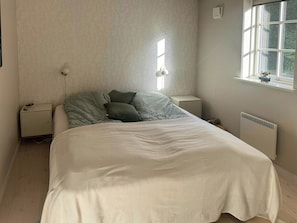Ein Schlafzimmer mit einem Bett, zwei Nachttischen, einer Heizung und einem Fenster.