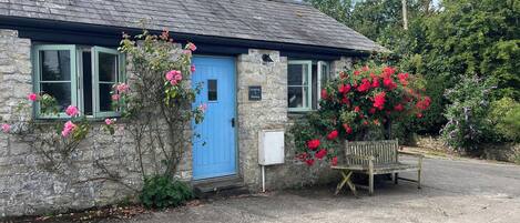 A stone building with a blue door, a bench outside, and a sign indicating a room number.
