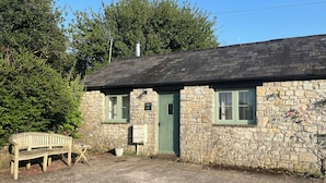 Une petite maison en pierre avec une porte verte, un banc et une petite table à l’extérieur.