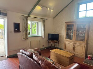 Una sala de estar con un sofá de cuero, una mesa de centro de madera, un televisor, un aparador con libros y una ventana con cortinas.