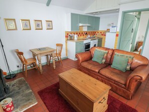 Una sala de estar con un sofá de cuero marrón, una mesa de centro de madera, una mesa de comedor con sillas y una kitchenette al fondo.
